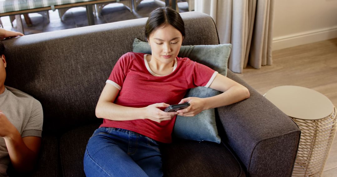Young Woman Seated on Sofa Using Smartphone in Relaxed Setting
