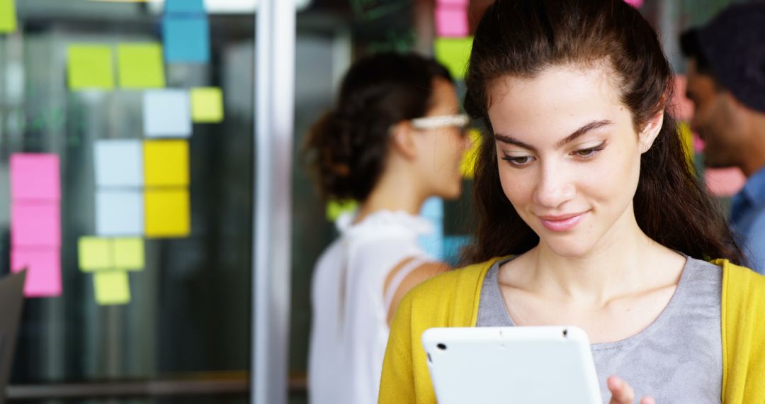 Young Woman Using Digital Tablet in Office With Sticky Notes in Background - Free Images, Stock Photos and Pictures on Pikwizard.com