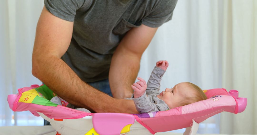 Father Carefully Placing Infant in Vibrant Baby Bouncer at Home - Free Images, Stock Photos and Pictures on Pikwizard.com