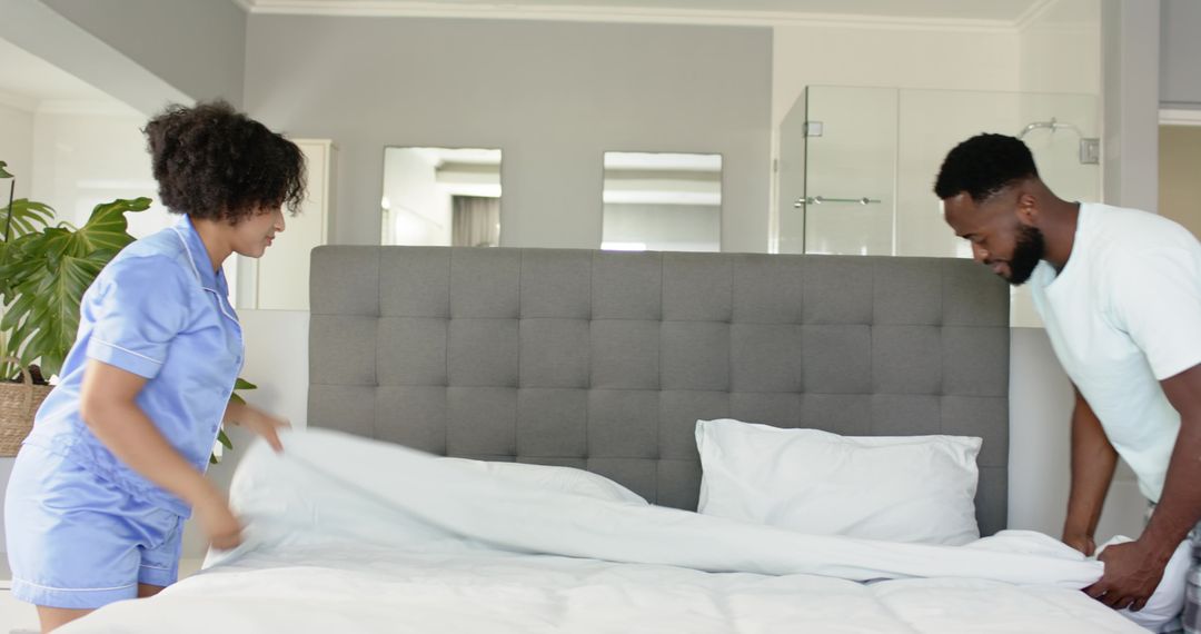 Couple making king-size bed with white duvet and crisp sheets in modern bedroom