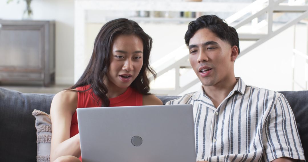 Asian couple sitting on sofa using laptop together sharing online shopping and planning