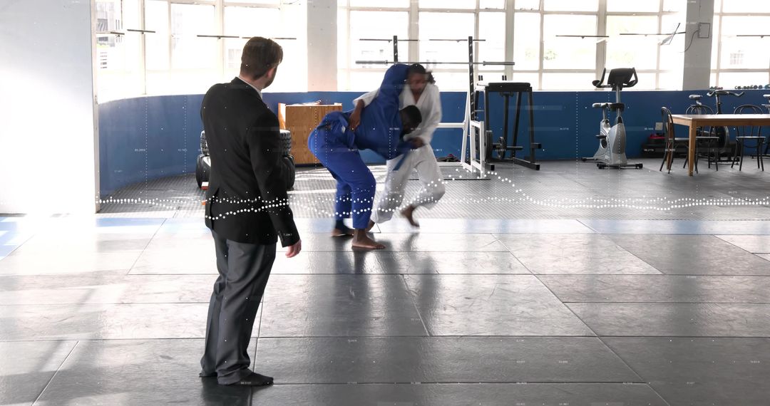 Instructor executing dynamic judo throw during martial arts training on padded mats in gym
