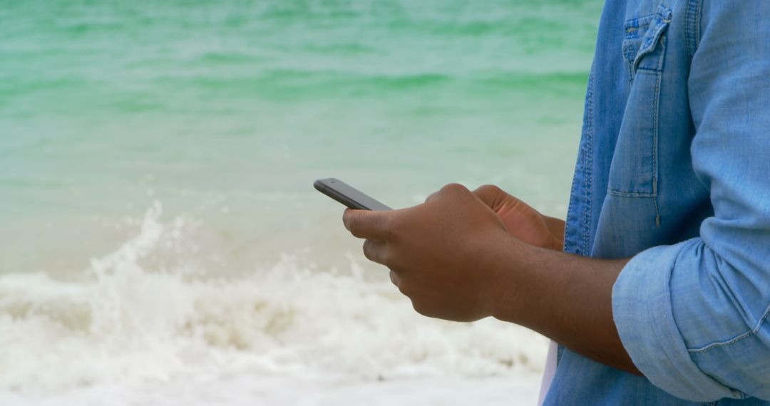 African American Man Texting on Beach with Ocean View