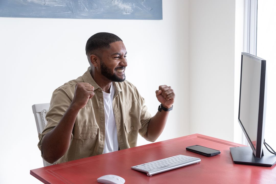 Excited Man Celebrating Success in Home Office Setup with Computer
