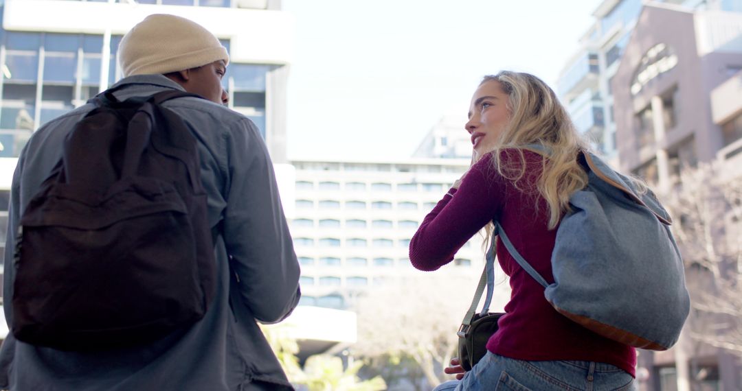 Multicultural young adults walking and talking in urban plaza with backpacks