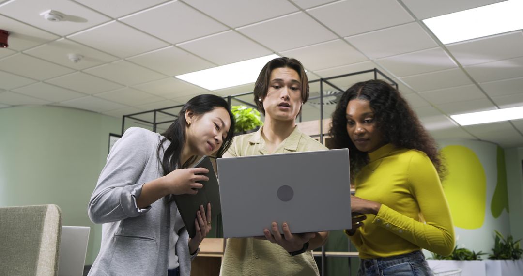 Diverse Coworkers Collaborating Over Laptop in Modern Office