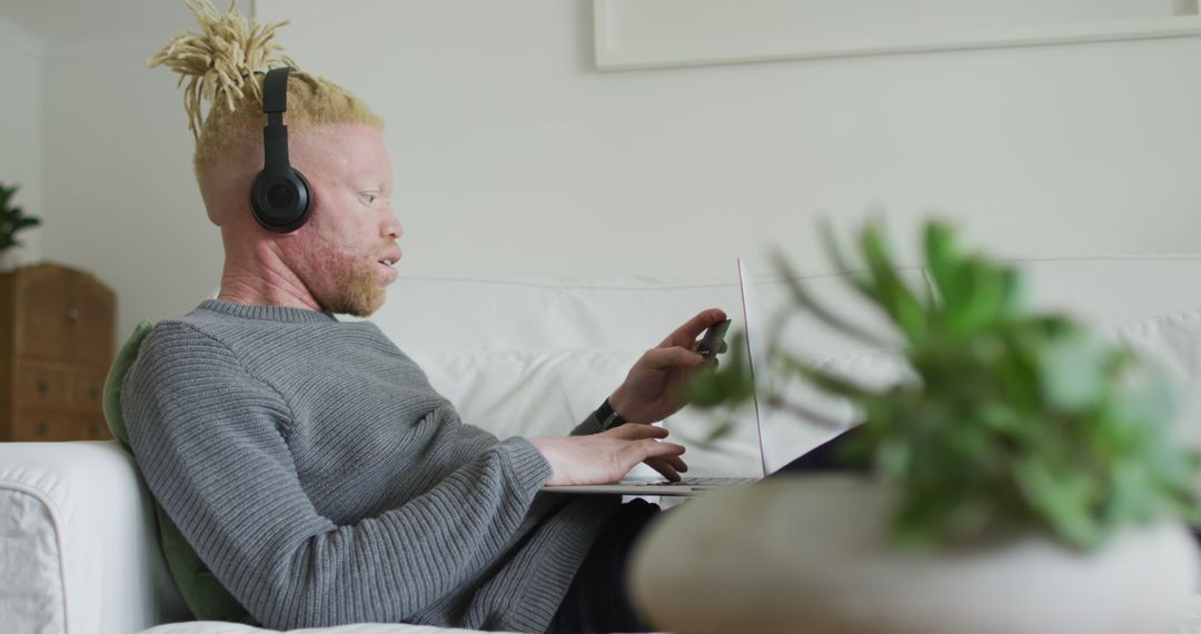 Young Albino Man Wearing Headphones Working on Laptop in Living Room - Free Images, Stock Photos and Pictures on Pikwizard.com