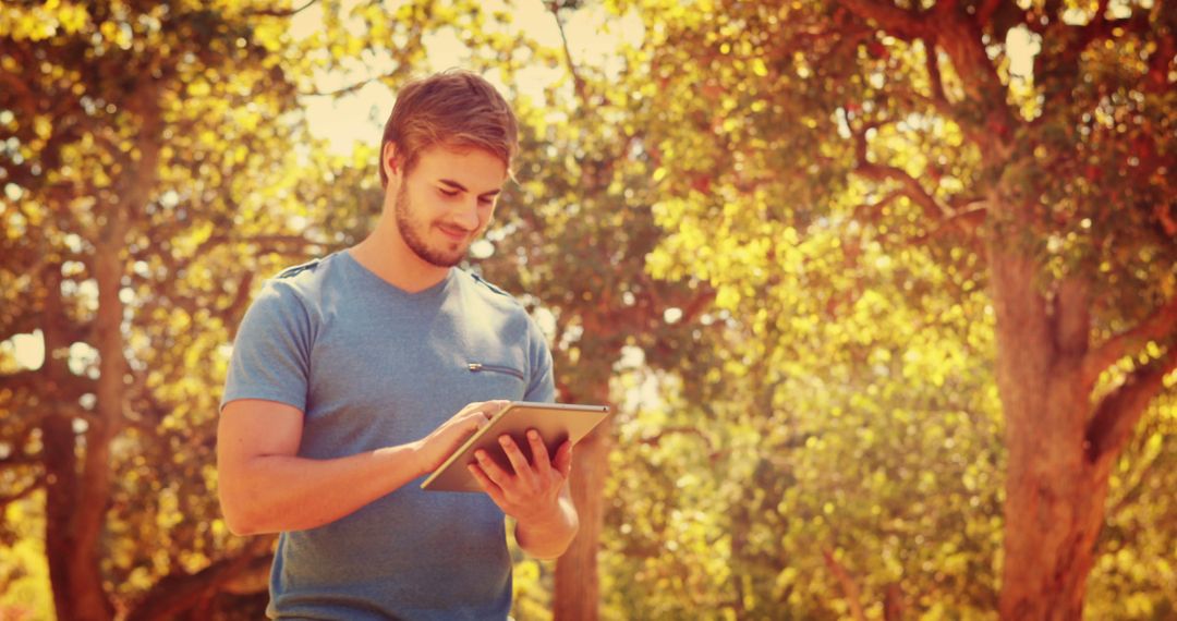 Young Man Using Tablet Outdoors in Sunlit Park - Free Images, Stock Photos and Pictures on Pikwizard.com