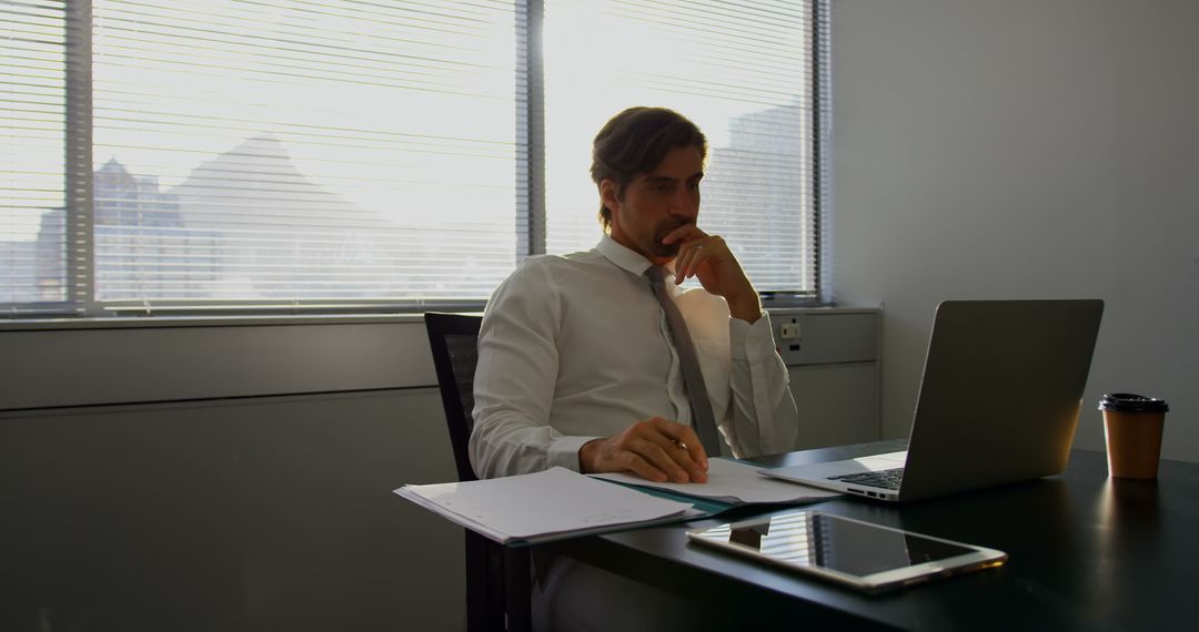 Thoughtful Executive Analyzing Reports on Laptop in Modern Office
