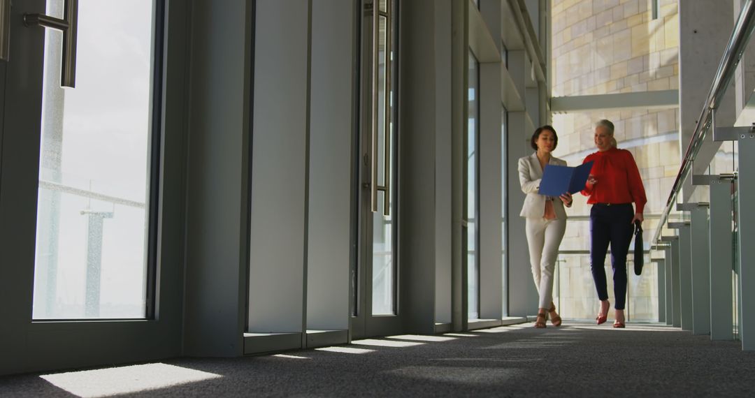 Businesswomen Discussing Documents in Sunlit Corridor