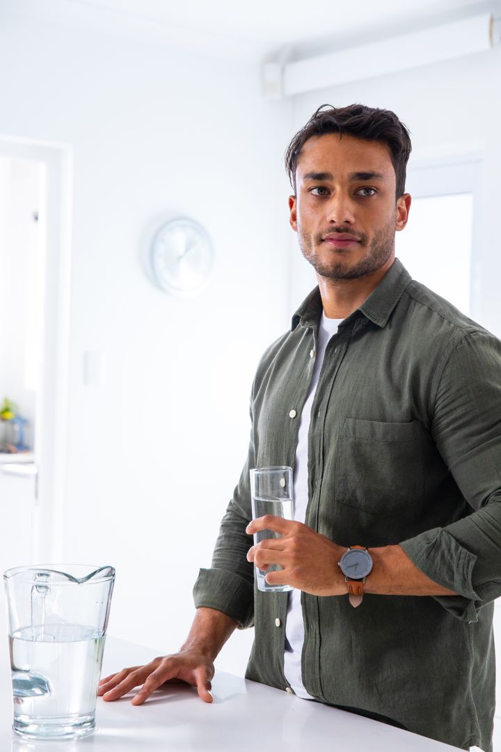 Man Enjoying Refreshing Drink in Modern White Kitchen