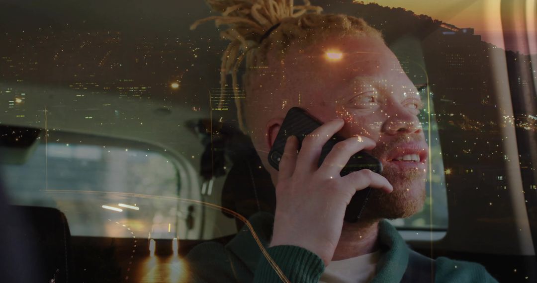 Smiling man with dreadlocks talking on smartphone in car at night with city reflections