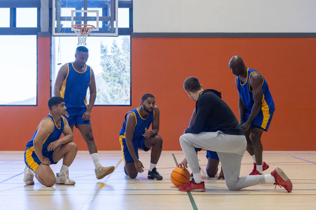 Diverse Basketball Team Strategizing with Coach in Gym
