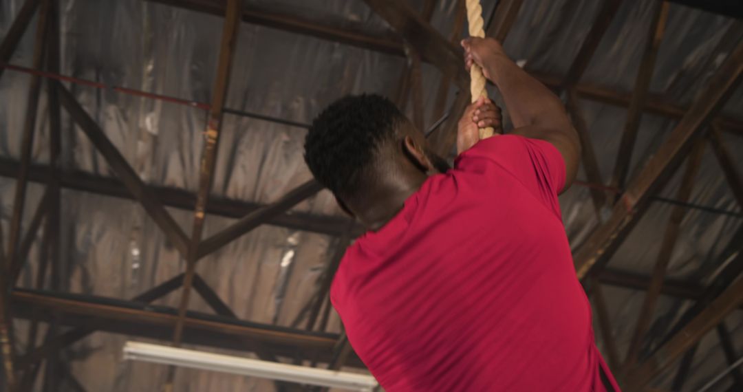 Determined Man Climbing Rope in Industrial Gym