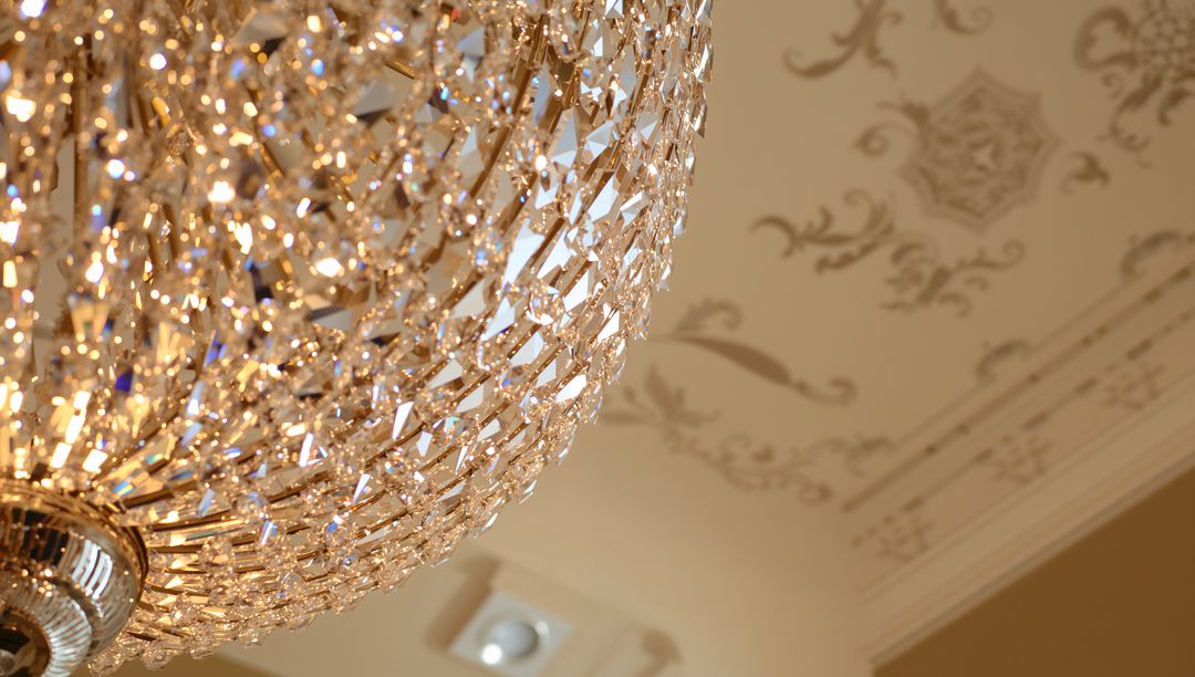 Glittering Crystal Chandelier Casting Golden Sparkle Against Ornate Plaster Ceiling