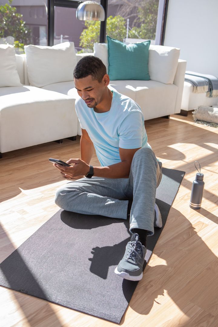 Man Relaxing with Smartphone on Mat in Bright Living Room