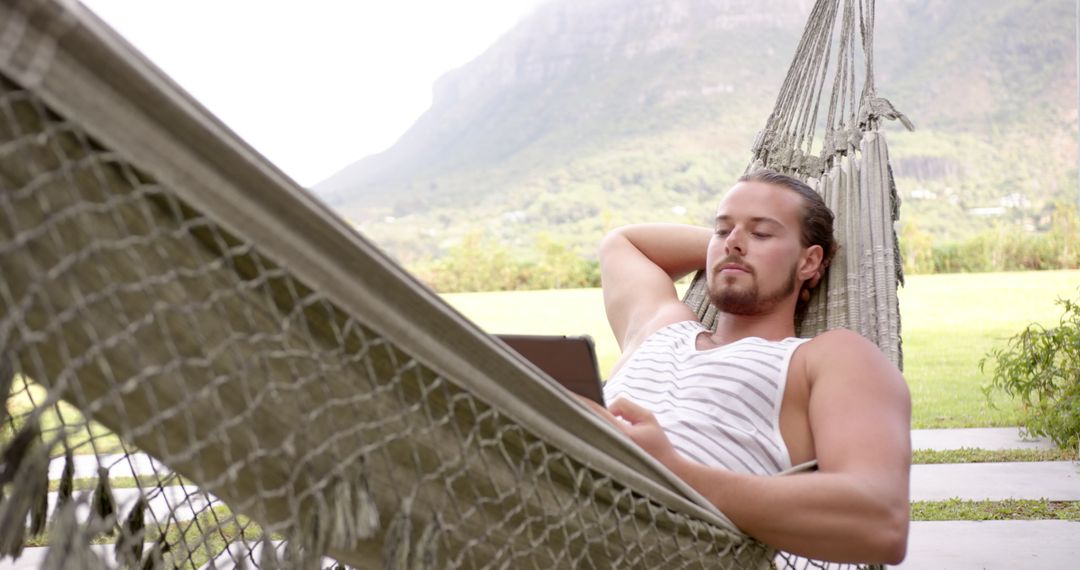 Young Man Relaxing in Hammock Using Tablet Outdoors