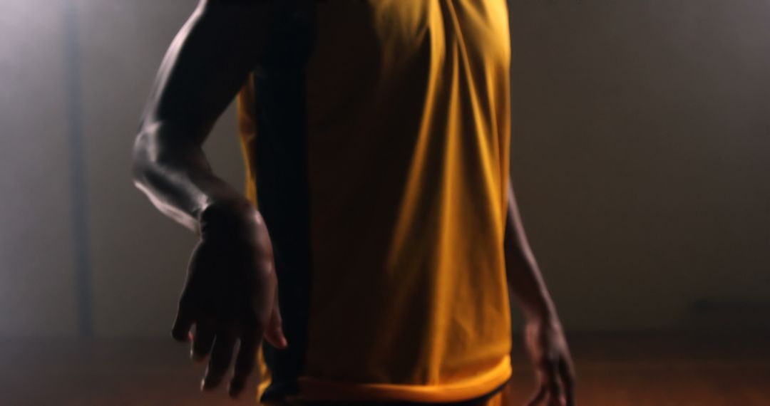 Fit Male Athlete Wearing Yellow Sports Jersey Flexing in Dark Ambient Lighting - Free Images, Stock Photos and Pictures on Pikwizard.com