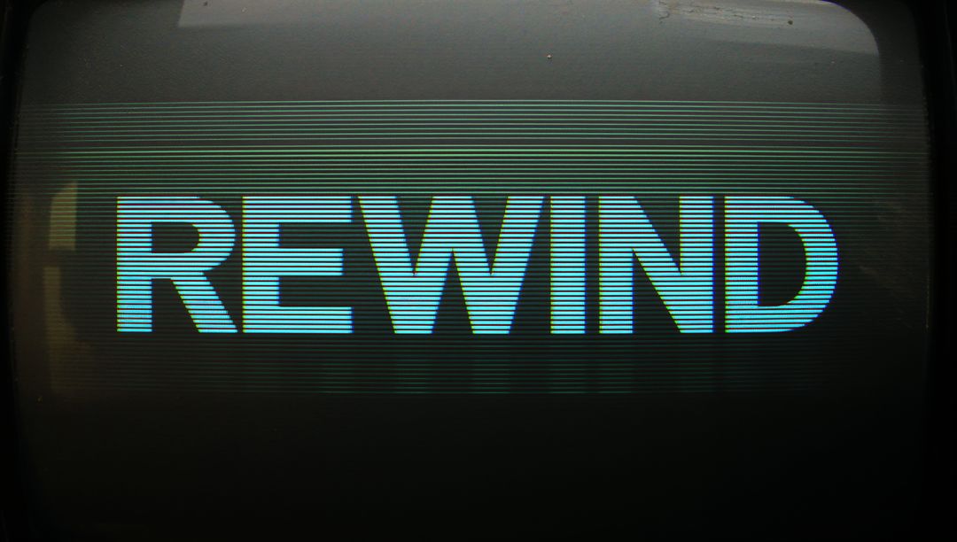 Vintage CRT Display Showing REWIND Text Glowing Cyan with Scanlines and Bezel Glare
