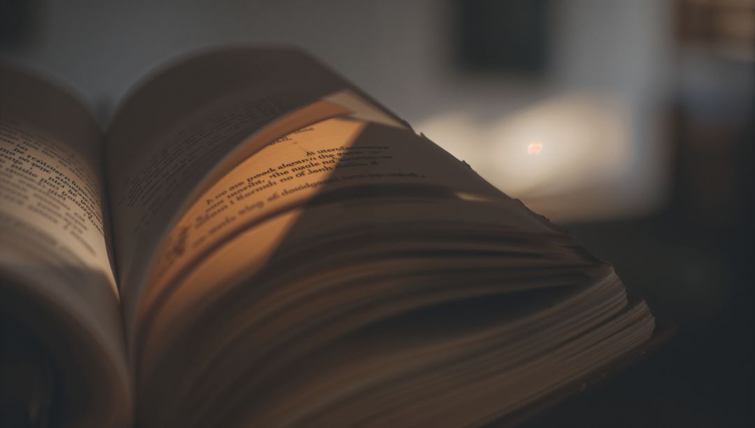 Open paperback with fanned pages and warm lamplight creating moody bokeh