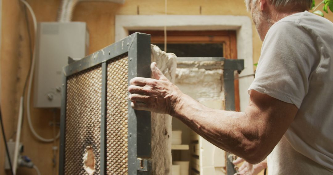 Senior Man Opening Kiln in Pottery Workshop