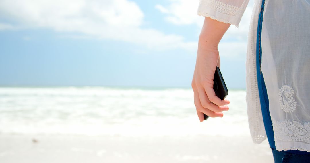 Woman Holding Smartphone Walking on Beach in Summer - Free Images, Stock Photos and Pictures on Pikwizard.com