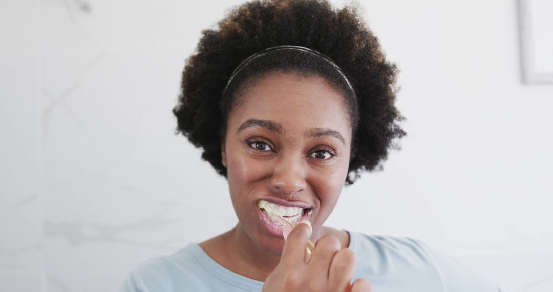 Smiling woman with curly hair brushing teeth in bathroom - Free Images, Stock Photos and Pictures on Pikwizard.com