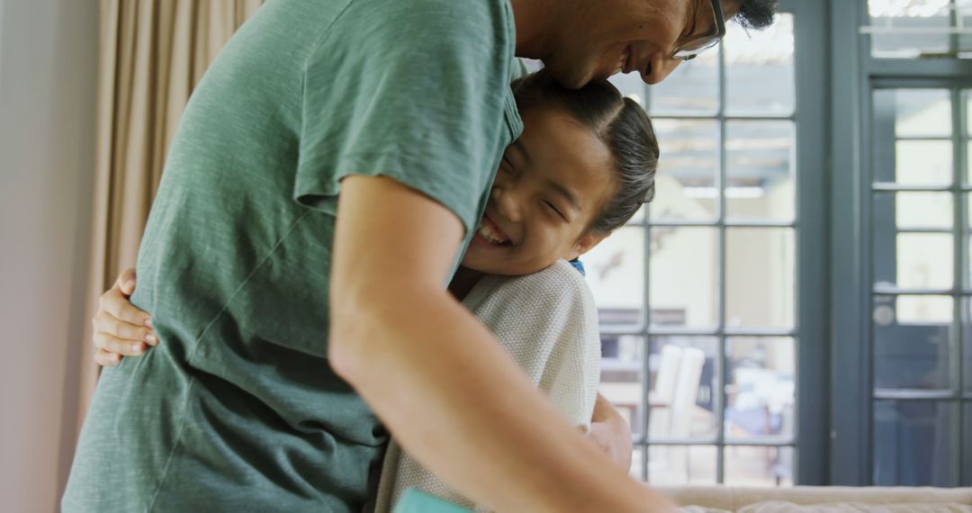 A young Asian girl shares a joyful hug with her father in a cozy indoor setting. - Free Images, Stock Photos and Pictures on Pikwizard.com