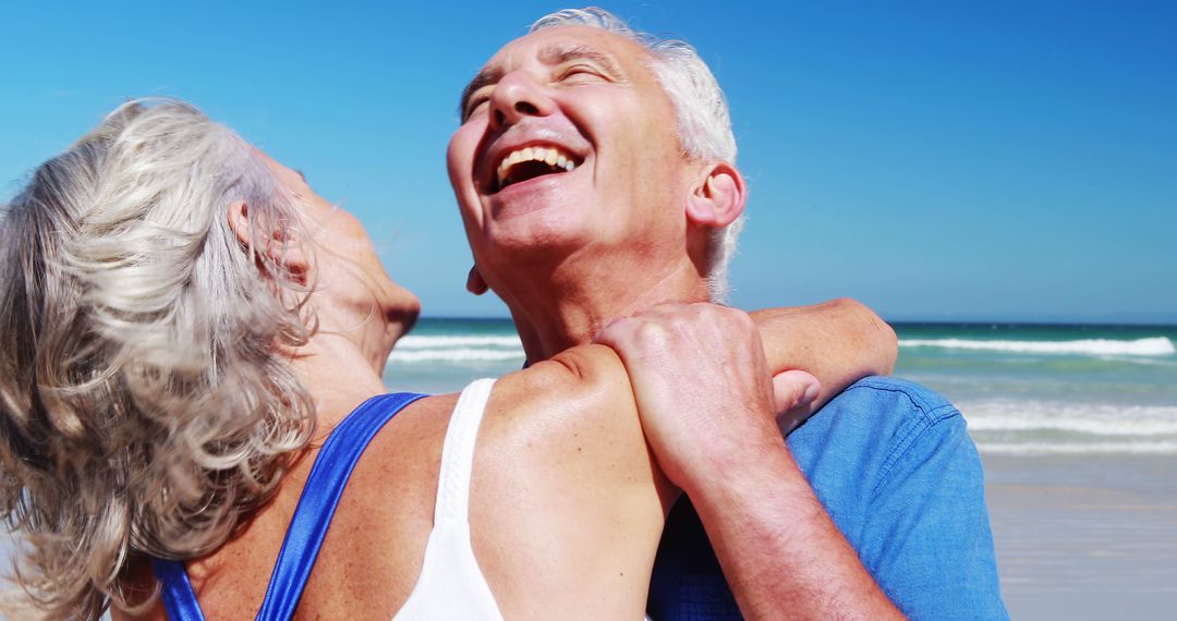 Senior Couple Embracing and Laughing at Beach on Sunny Day - Free Images, Stock Photos and Pictures on Pikwizard.com