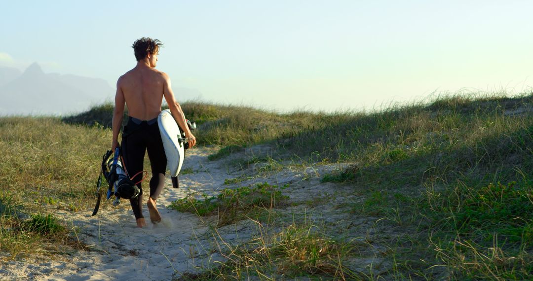 Back View of Male Surfer Walking on Sandy Path Through Dunes at Sunset - Free Images, Stock Photos and Pictures on Pikwizard.com