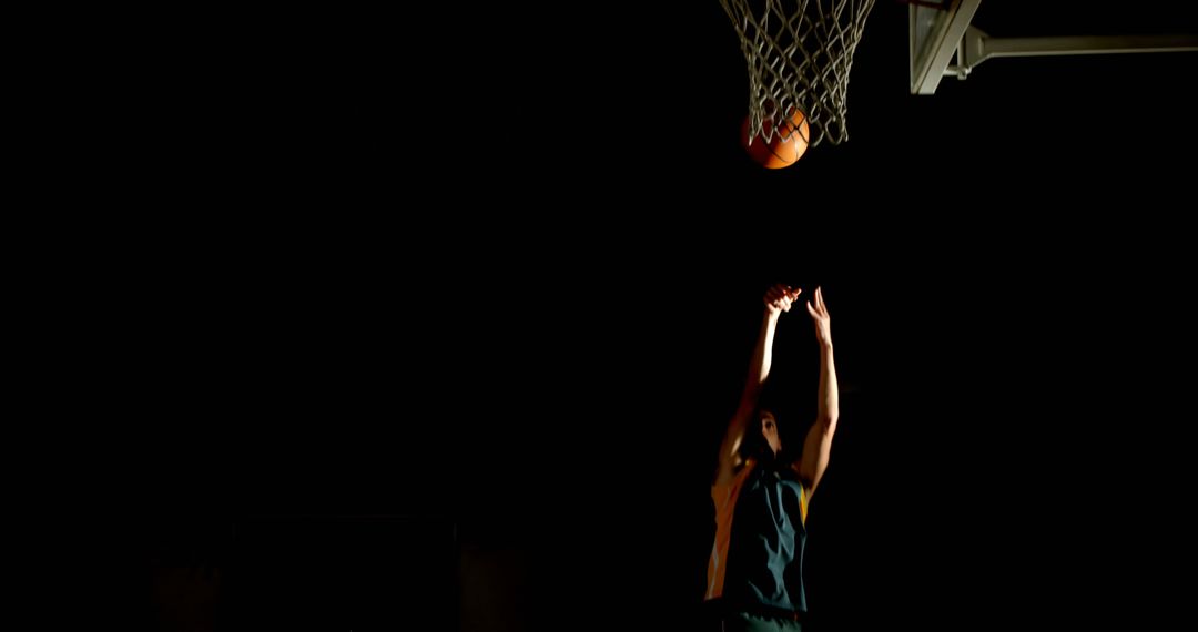 Basketball Player Shooting Hoop in Dimly Lit Gym