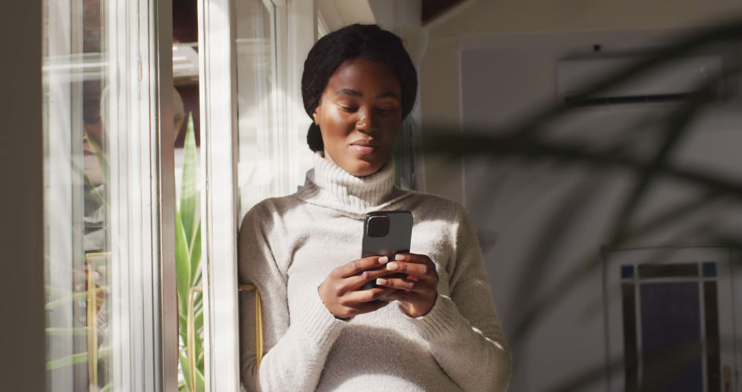 Young African American Woman Using Smartphone Near Window - Free Images, Stock Photos and Pictures on Pikwizard.com