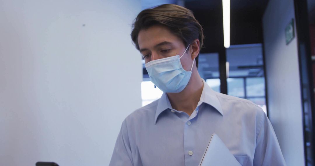 Professional Man with Mask Checking Smartphone in Office Corridor