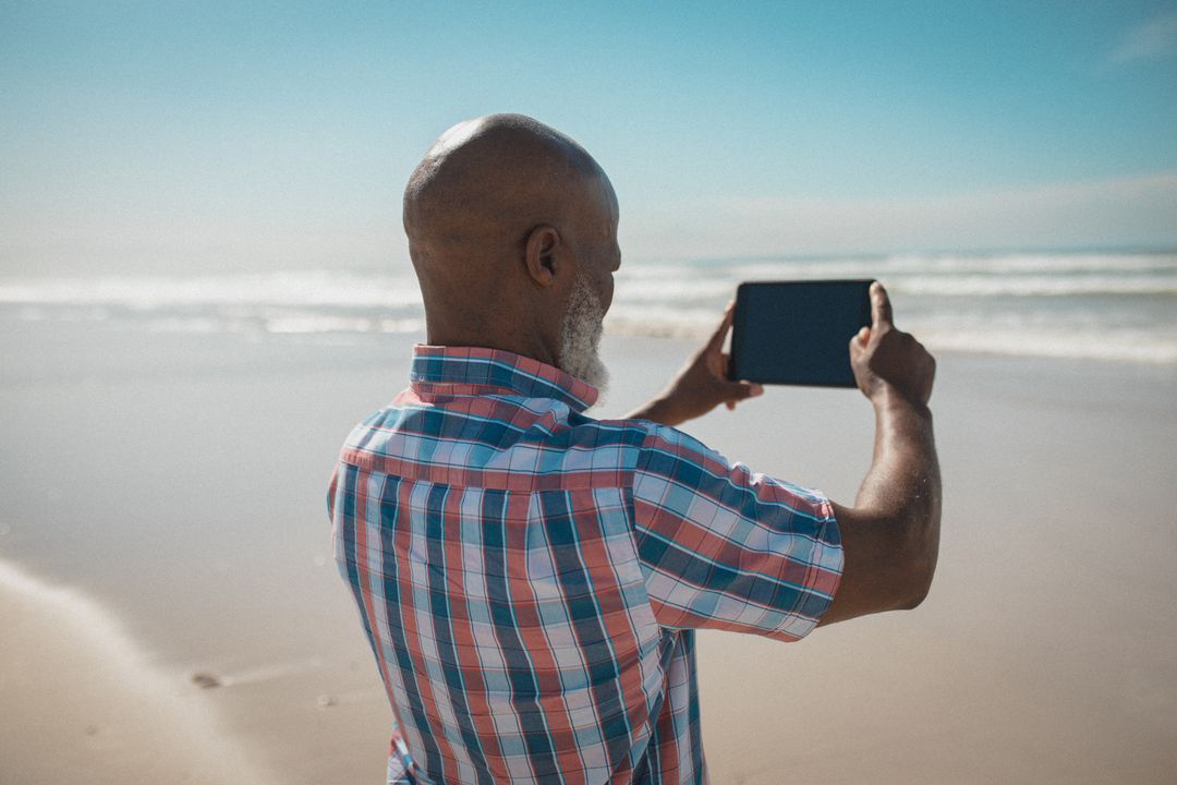 African american senior male standing on beach and taking picture - Free Images, Stock Photos and Pictures on Pikwizard.com