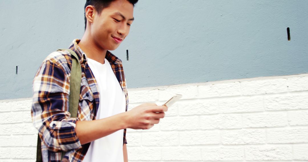 Young man texting on smartphone while walking on city sidewalk - Free Images, Stock Photos and Pictures on Pikwizard.com