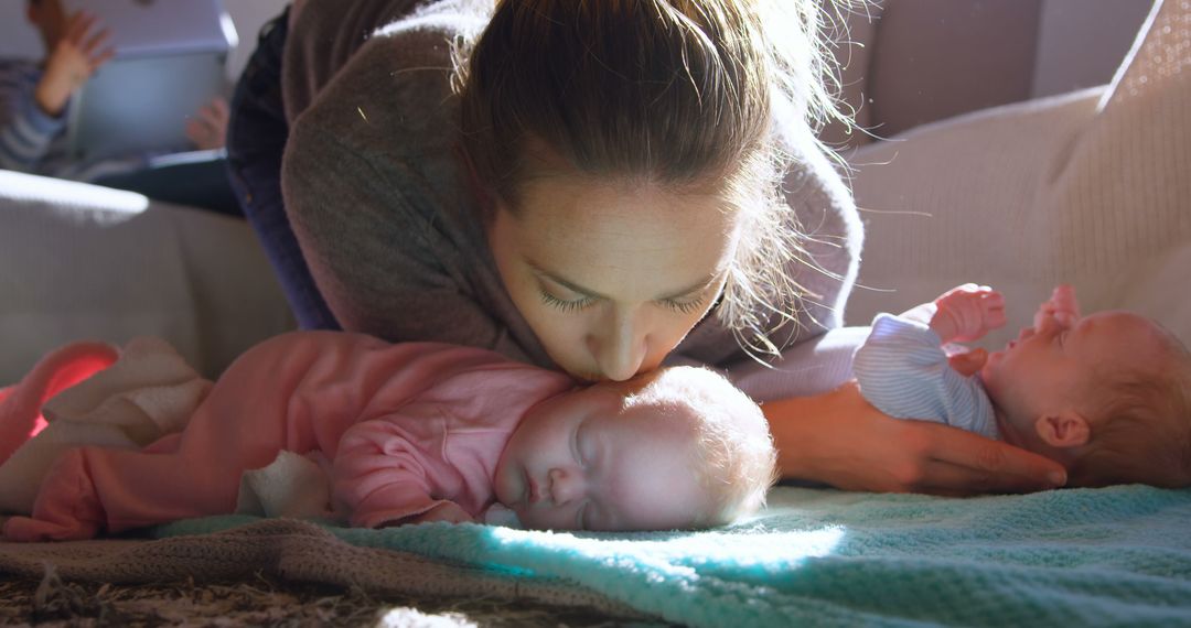 A Caucasian woman gently kisses a sleeping infant while another baby lies nearby, with copy space - Free Images, Stock Photos and Pictures on Pikwizard.com