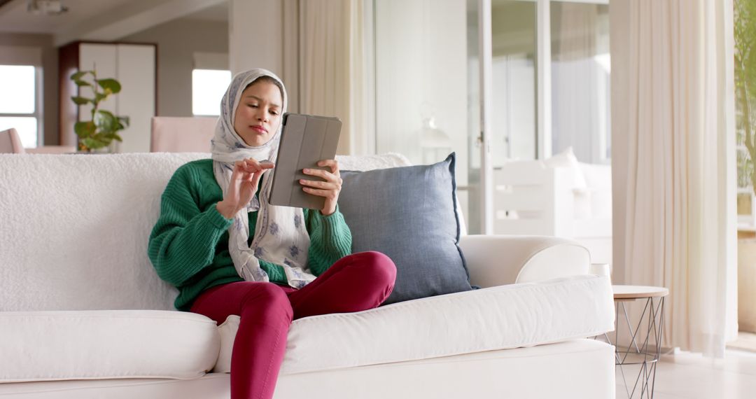 Young Woman in Hijab Browsing Tablet on Couch at Home - Free Images, Stock Photos and Pictures on Pikwizard.com