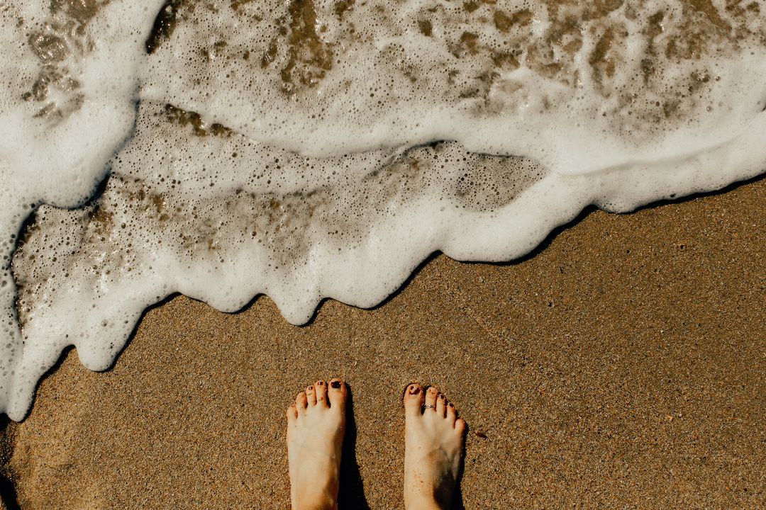 Standing barefoot on sandy beach with incoming foamy wave
