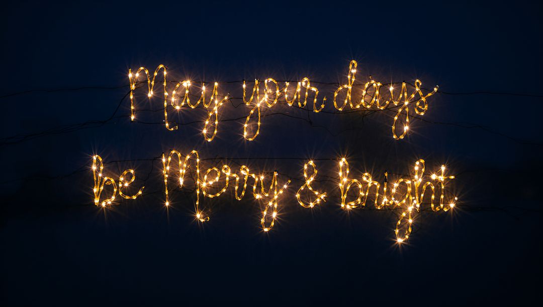 May Your Days Be Merry & Bright glowing LED script casting warm starbursts on dark sky