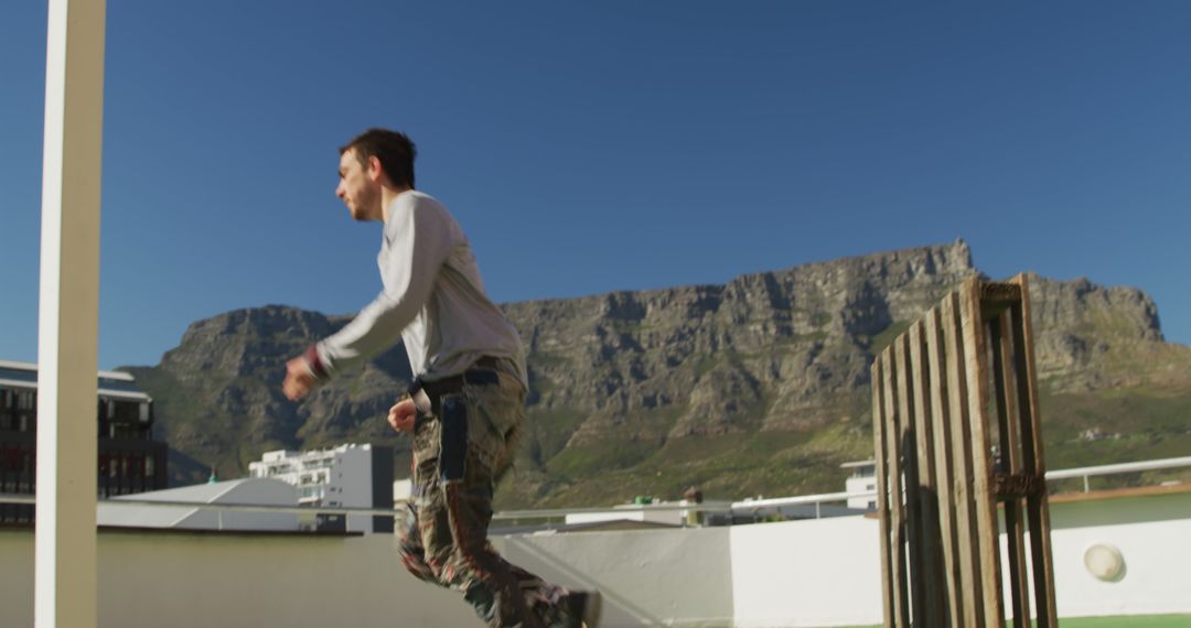 Man Engaging in Parkour on Urban Rooftop with Mountain View - Free Images, Stock Photos and Pictures on Pikwizard.com