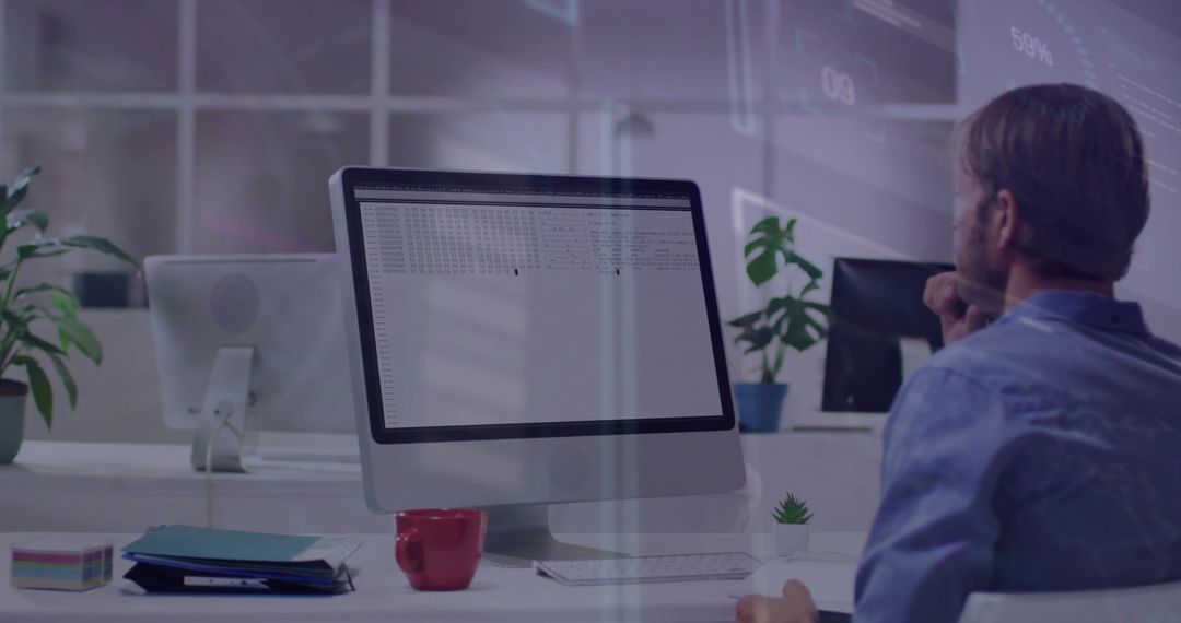 Man analyzing spreadsheet on desktop monitor in modern open-plan office concentrating on data