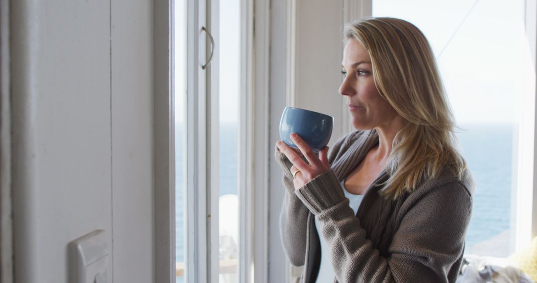 Woman Relaxing with Morning Coffee by Window Overlooking Ocean - Free Images, Stock Photos and Pictures on Pikwizard.com