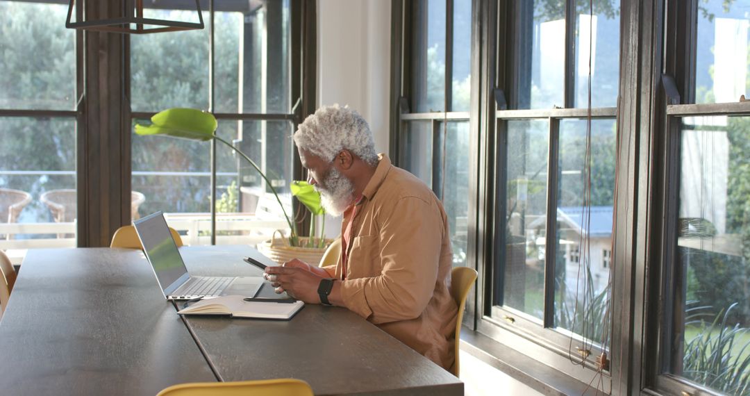 Senior Man Using Laptop and Phone in Bright Home Office
