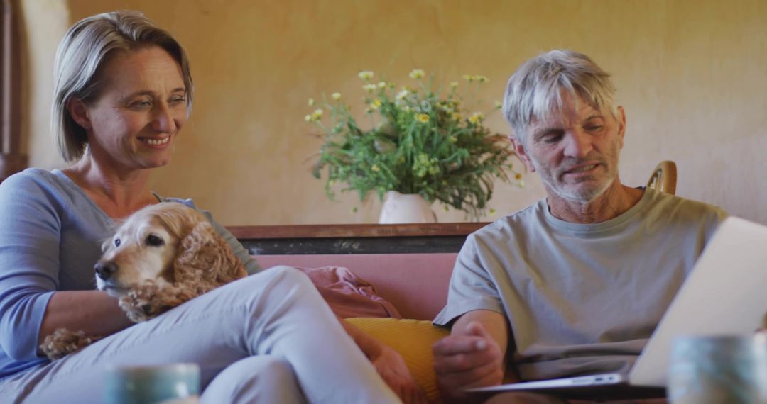 Senior Couple Relaxing with Dog Using Laptop on Comfortable Sofa