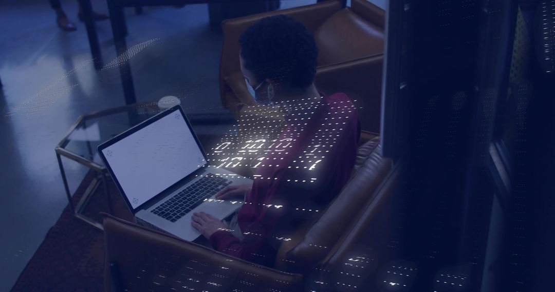 Woman working on laptop in lounge wearing face mask with dotted light projection