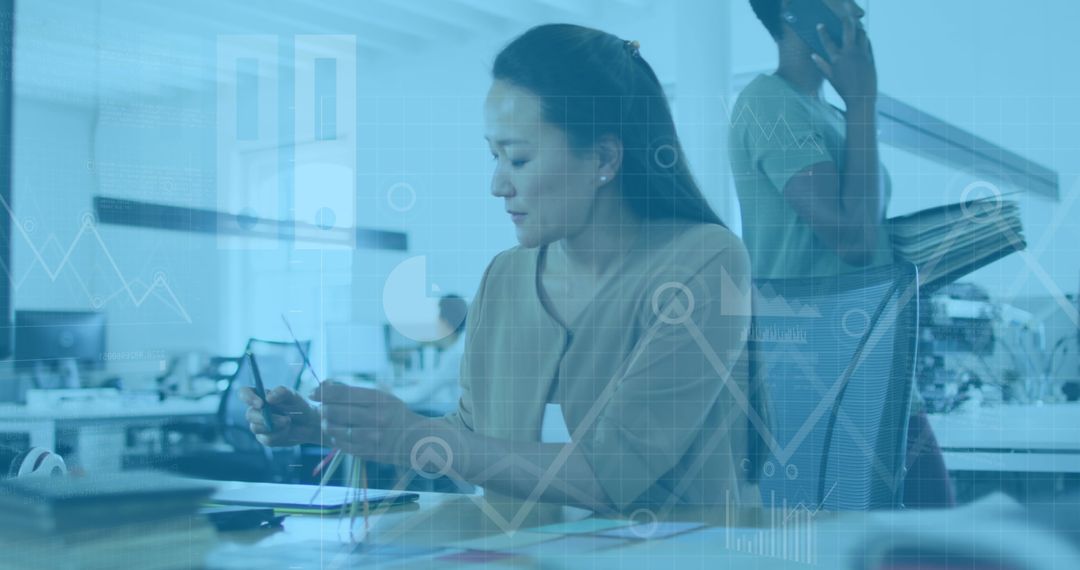Asian Woman Analyzing Data with Digital Graphics Overlay in Modern Office