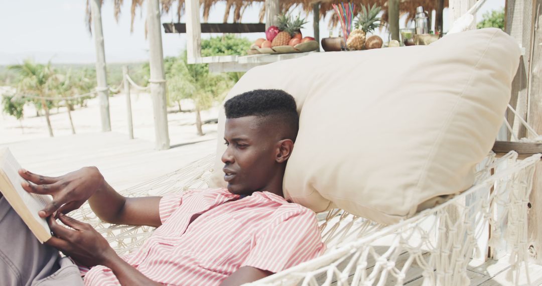 Young Man Relaxing on Tropical Beach Hammock Reading Book - Free Images, Stock Photos and Pictures on Pikwizard.com