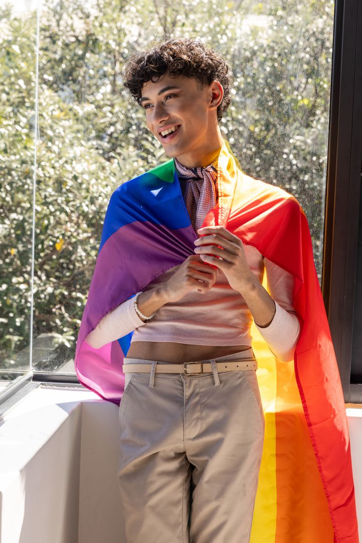 Smiling Man Draped in Pride Flag Embracing Sunlit Interior Moment