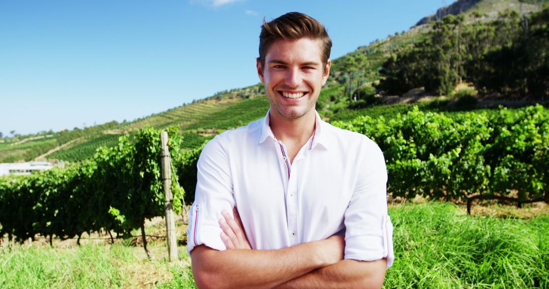 Smiling Man Standing in Sunlit Vineyard with Arms Crossed