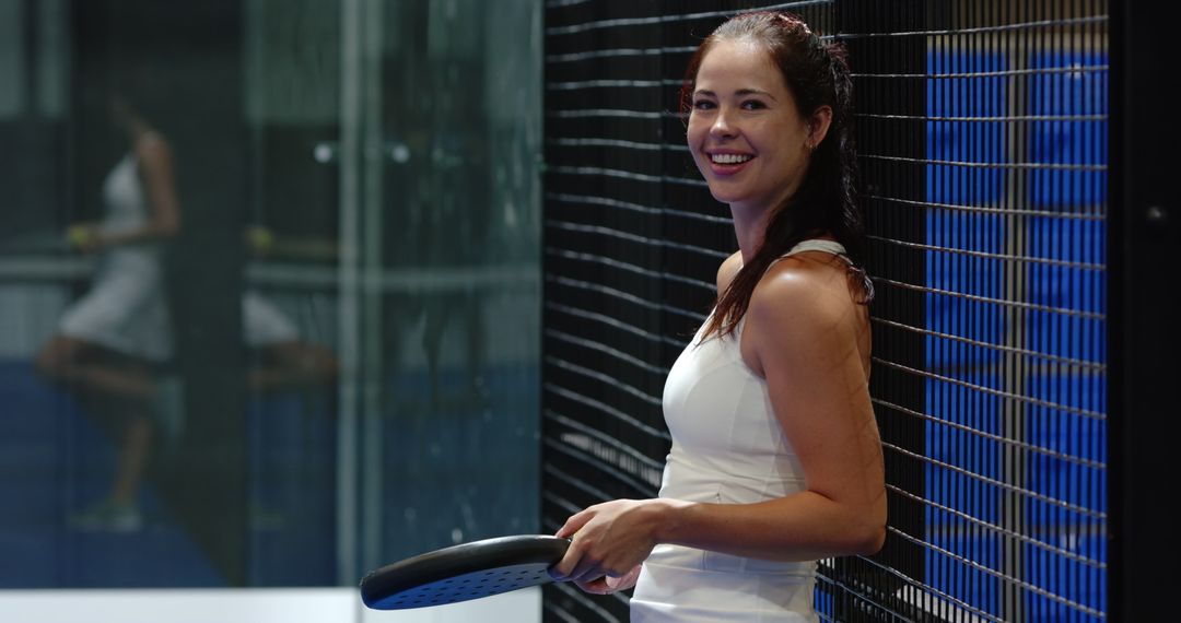 Female Padel Athlete Leaning on Court Net with Racket Smiling